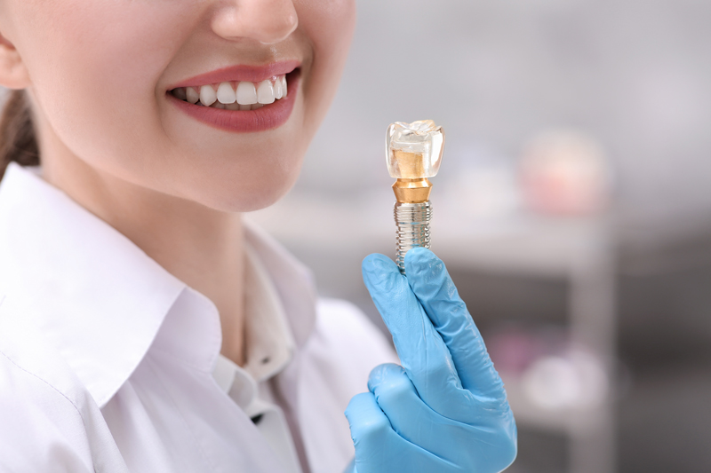 Dentist holding educational model of dental implant indoors, closeup